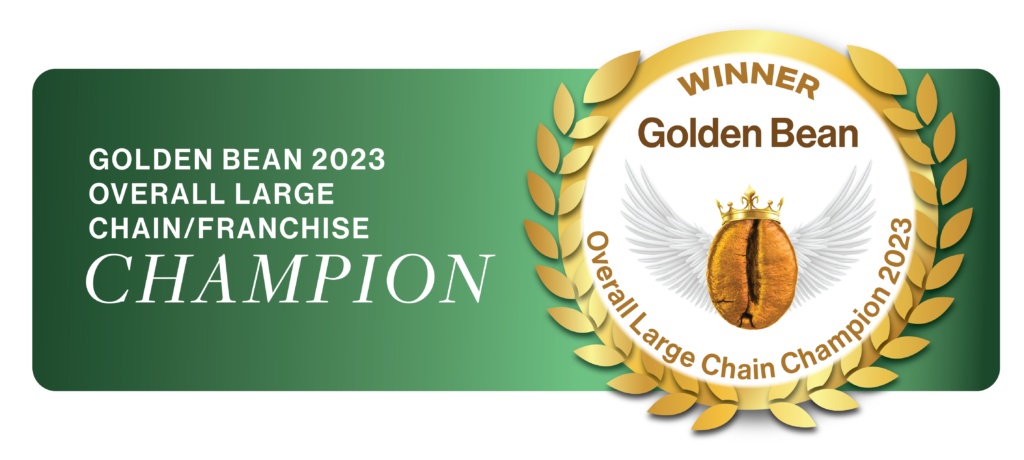 A banner announces the Golden Bean Award 2023 for Overall Large Chain/Franchise Champion. A golden wreath surrounds a coffee bean with wings and a crown, with "Winner Golden Bean" and "Overall Large Chain Champion 2023" written on it.